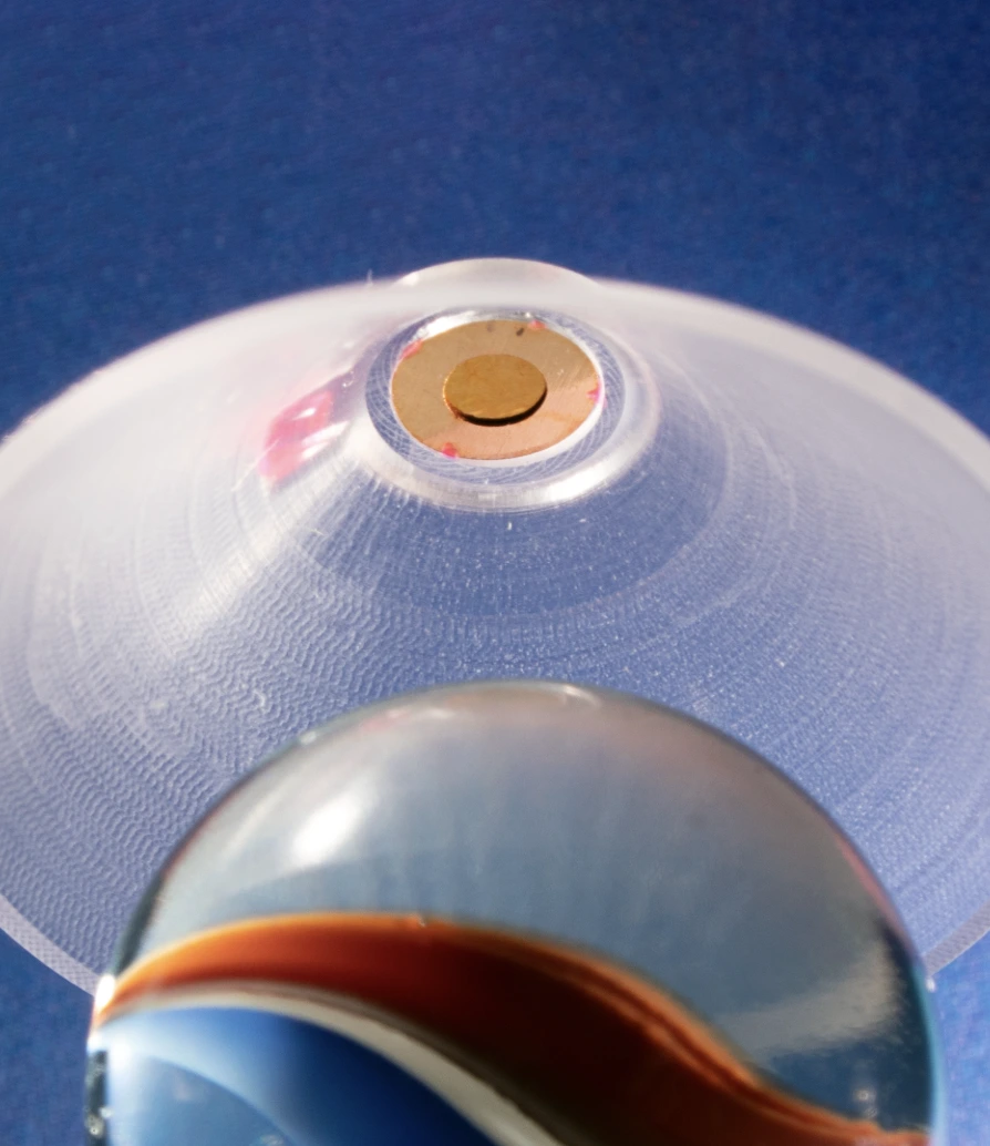 Acrylic cone target with a small gold disk in its center photographed with a marble with a blue background.